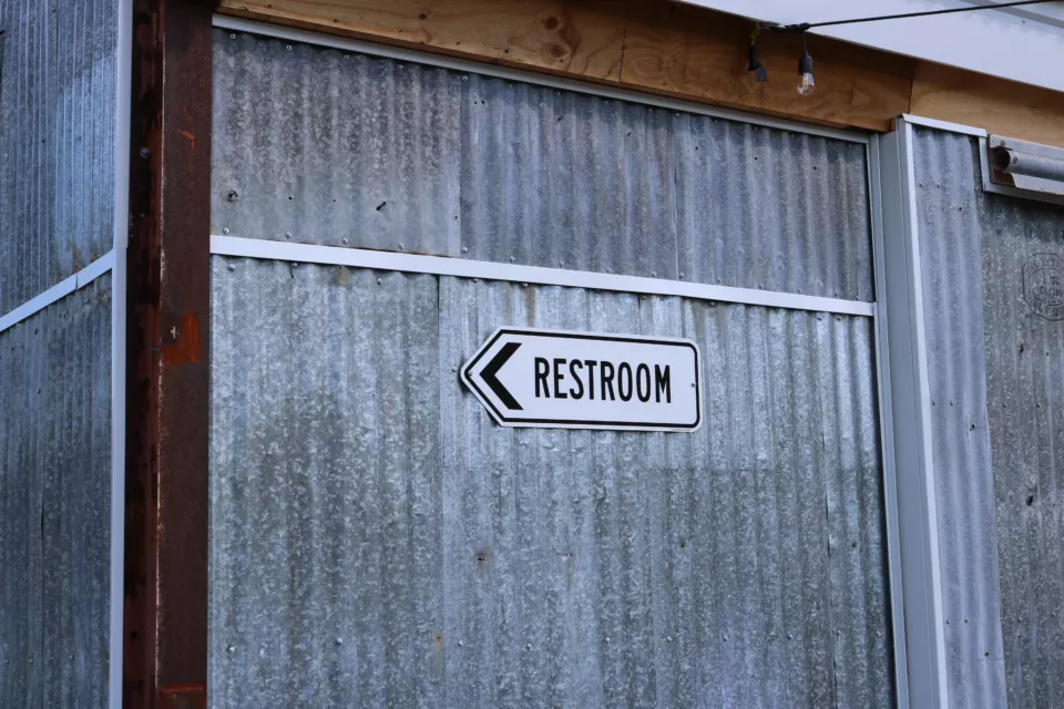 A Restroom Sign Hanging on a Corrugated Metal Wall